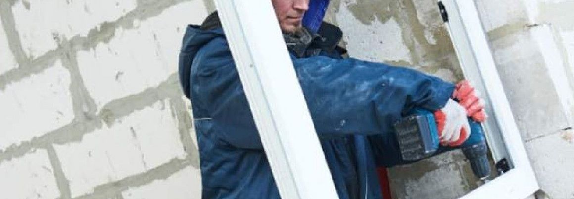 Person verschraubt Fensterrahmen in Mauerwerk